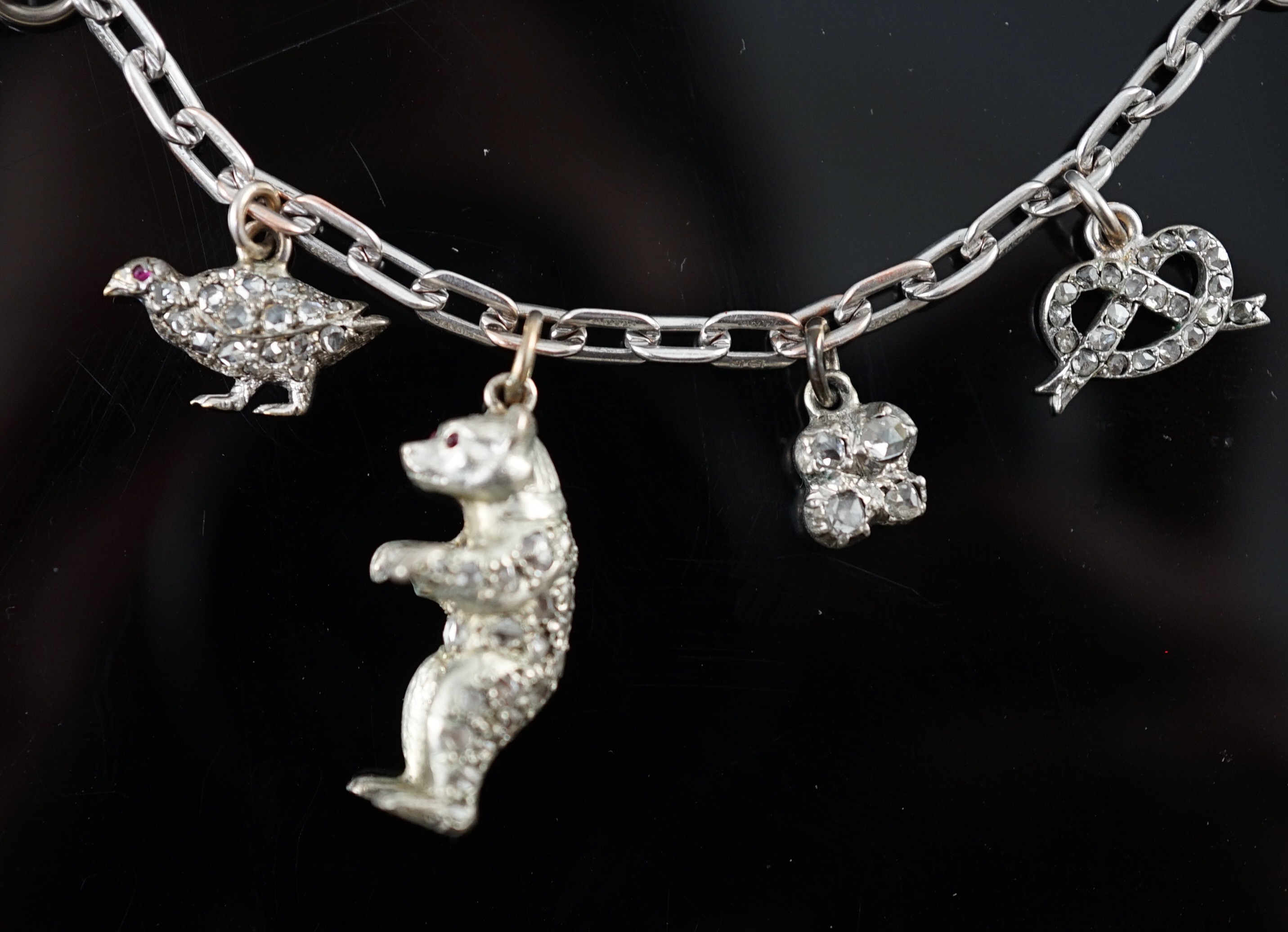 A 9ct white gold charm bracelet, with French platinum and diamond set clasp and hung with nine assorted charms, eight set with diamonds